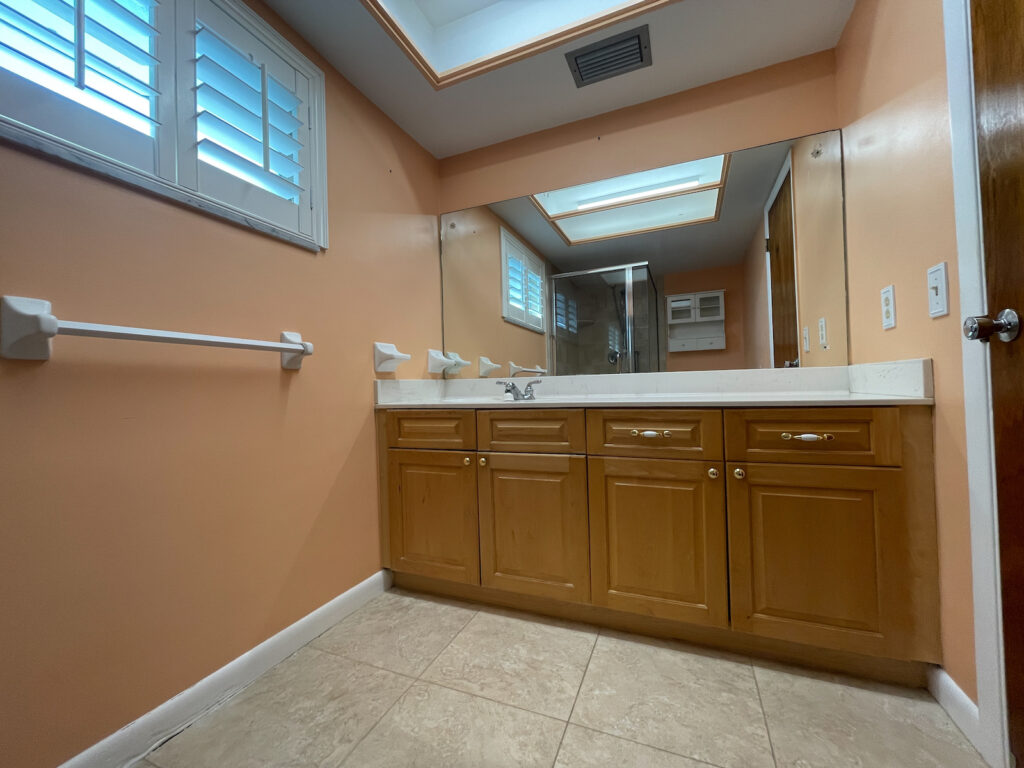 Outdated builder-grade bathroom with peach walls and wood vanity before remodel in Treasure Island